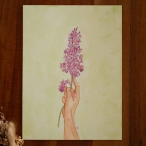 Aquarelle originale d'une main de femme tenant une branche de fleurs de lilas violettes sur fond vert. L'œuvre s'intitule Selon sa saison. Elle est créée par une artiste québécoise. L'aquarelle explore le thème de la comparaison. L'œuvre est un doux rappel que tu n'as pas besoin de fleurir comme els autres pour être exactement là où tu dois être.