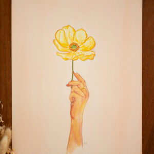 Aquarelle d'une main de femme tenant une fleur d'anémone jaune sur fond rose. L'œuvre s'intitule Porteuse de bonheur. Elle est créée par l'artiste québécoise Roxanne Bédard. L'aquarelle évoque les moments de joie et de plénitude que nous portons en nous.