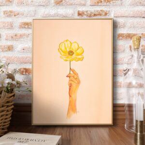 Aquarelle d'une main de femme tenant une fleur d'anémone jaune sur fond rose. L'œuvre s'intitule Porteuse de bonheur. Elle est créée par l'artiste québécoise Roxanne Bédard. L'aquarelle évoque les moments de joie et de plénitude que nous portons en nous.